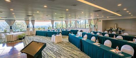 A conference room with multiple tables, chairs, and a stage area.