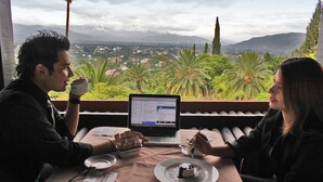 A couple dining at a table with a laptop, a dessert plate, and a cup of coffee, overlooking a cityscape with mountains and palm trees. - Hotel Victoria Oaxaca (Oaxaca)