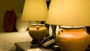 A hotel room with a bed, a nightstand with a lamp, a telephone, and a vase.