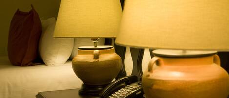Et hotelværelse med en seng, et sengebord med lampe, en telefon og en vase.