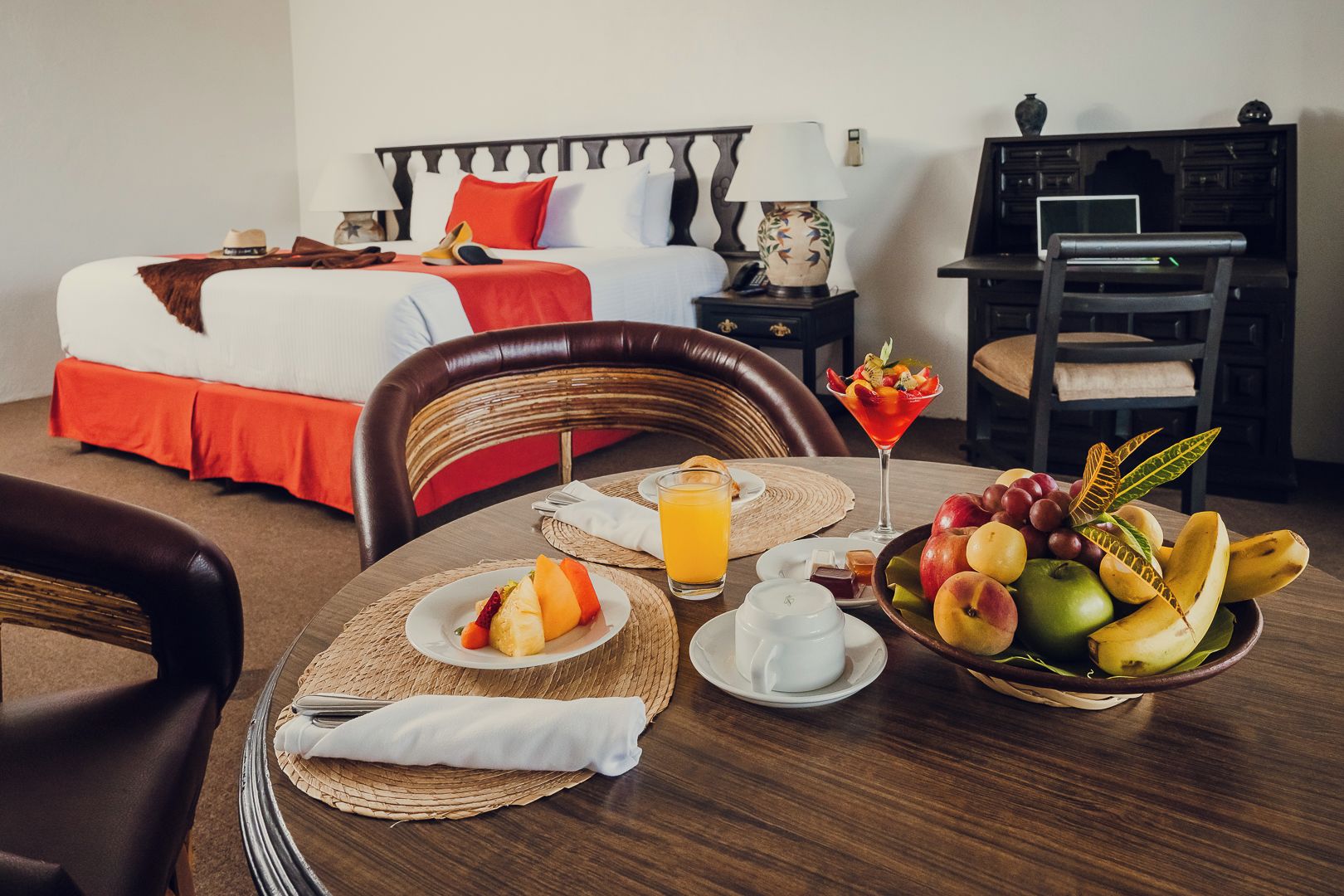 Habitación de hotel con cama, mesita de noche, lámpara y una mesa de comedor con el desayuno servido.