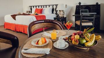 Habitación de hotel con cama, mesita de noche, lámpara y una mesa de comedor con el desayuno servido.