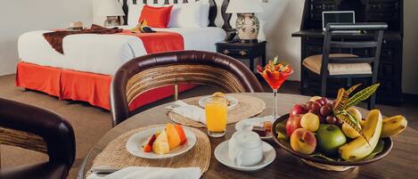 Habitación de hotel con cama, mesita de noche, lámpara y una mesa de comedor con el desayuno servido.