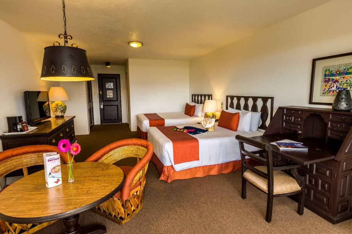 Habitación de hotel con dos camas, una mesa de comedor, una silla, un escritorio y una lámpara.