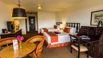 A hotel room with two beds, a dining table, a chair, a desk, and a lamp.