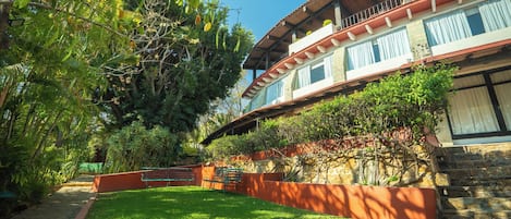 A two-story building with a stone facade, a balcony with plants, and a well-maintained lawn.