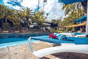 Un área junto a la piscina con sillones de descanso, un arreglo floral y palmeras.