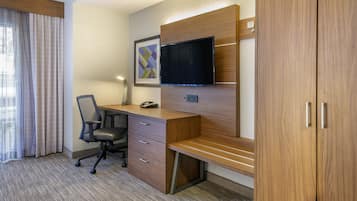 A hotel room with a wooden desk, a chair, a flat-screen TV mounted on the wall, and a large wardrobe.