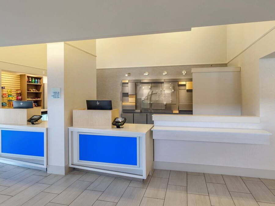 Zona de recepción de un hotel con mostrador de registro, quiosco de auto-servicio y una pequeña área de cocina.