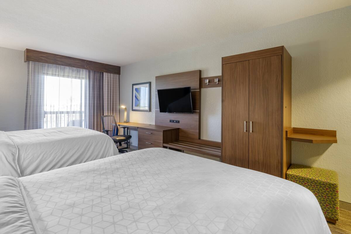 A hotel room with two beds, a desk, a television, and a wardrobe.
