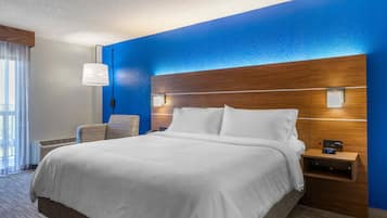 A hotel room with a large bed, a wooden headboard, a nightstand with a clock, and a chair.