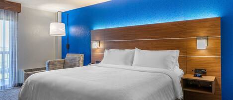 A hotel room with a large bed, a wooden headboard, a nightstand with a clock, and a chair.