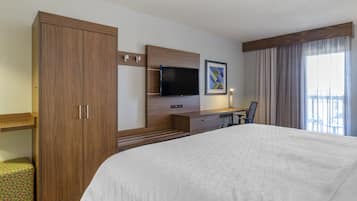 A hotel room with a large bed, a desk with a flat-screen TV, a wardrobe, and a window with curtains.