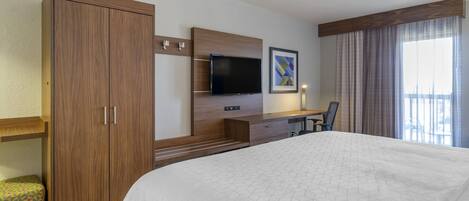 A hotel room with a large bed, a desk with a flat-screen TV, a wardrobe, and a window with curtains.