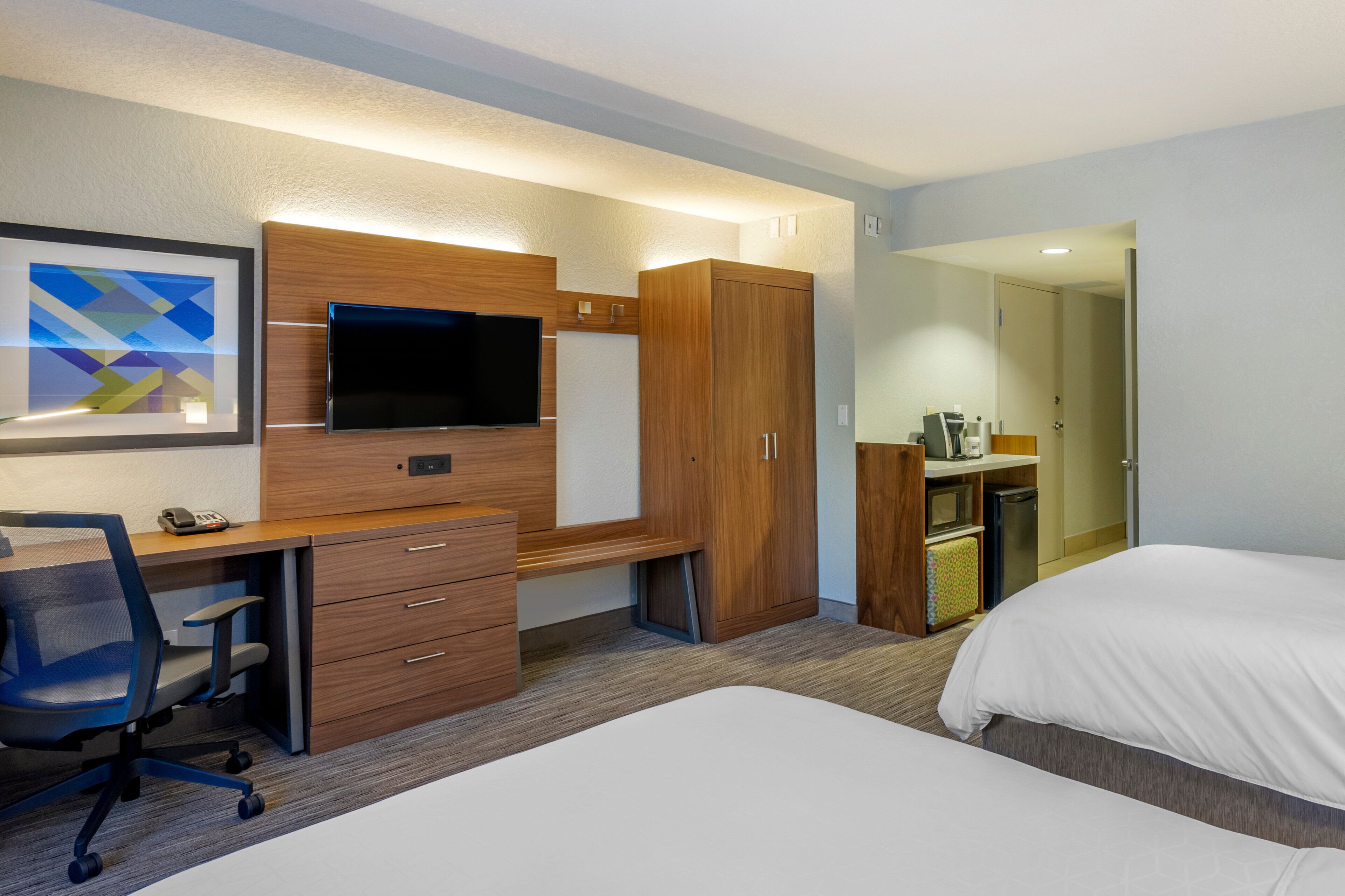 Habitación de hotel con escritorio, silla, televisión, armario y cama.