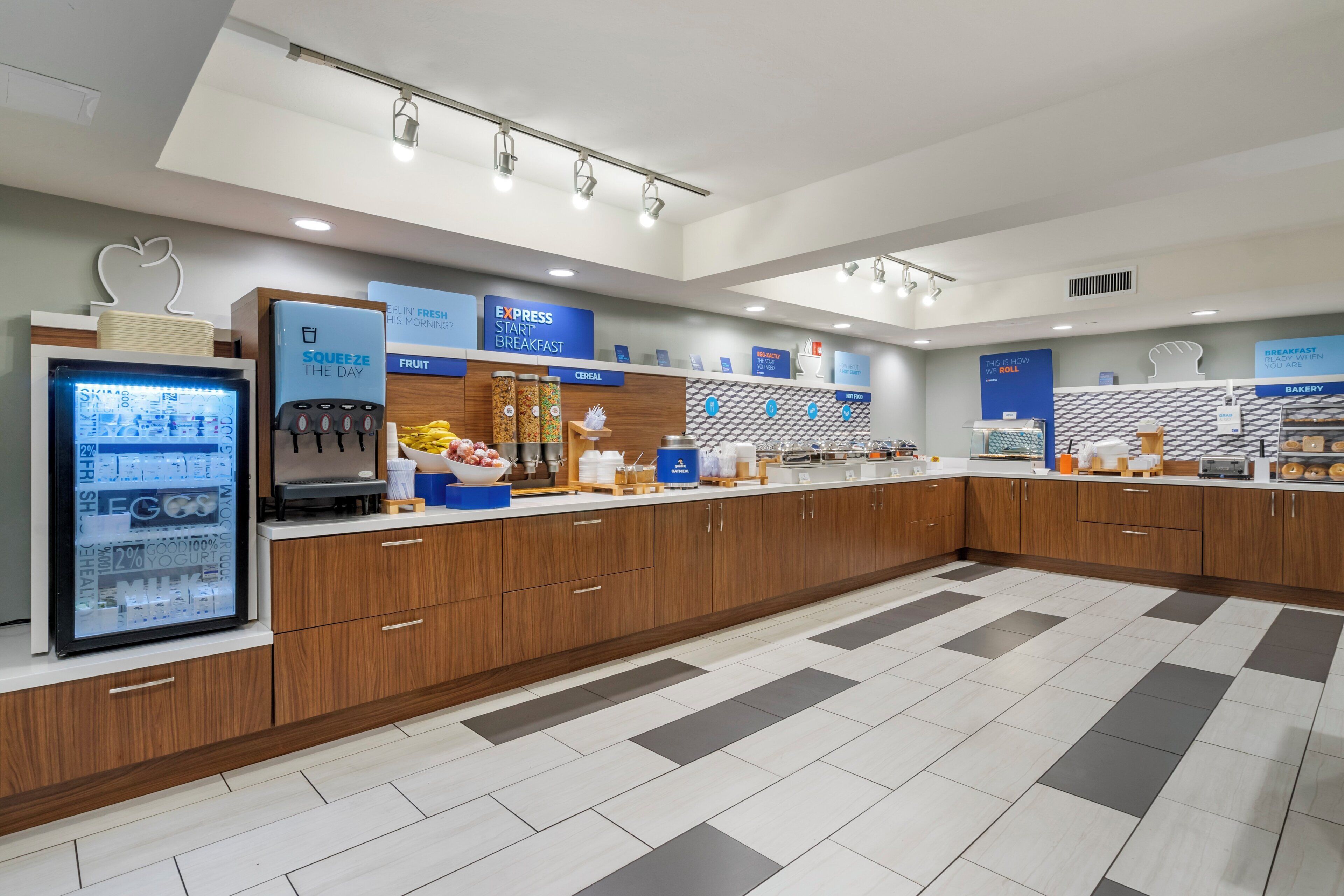 Un moderno comedor con servicio de buffet, un refrigerador con exhibición de yogures y diversas opciones de alimentos.