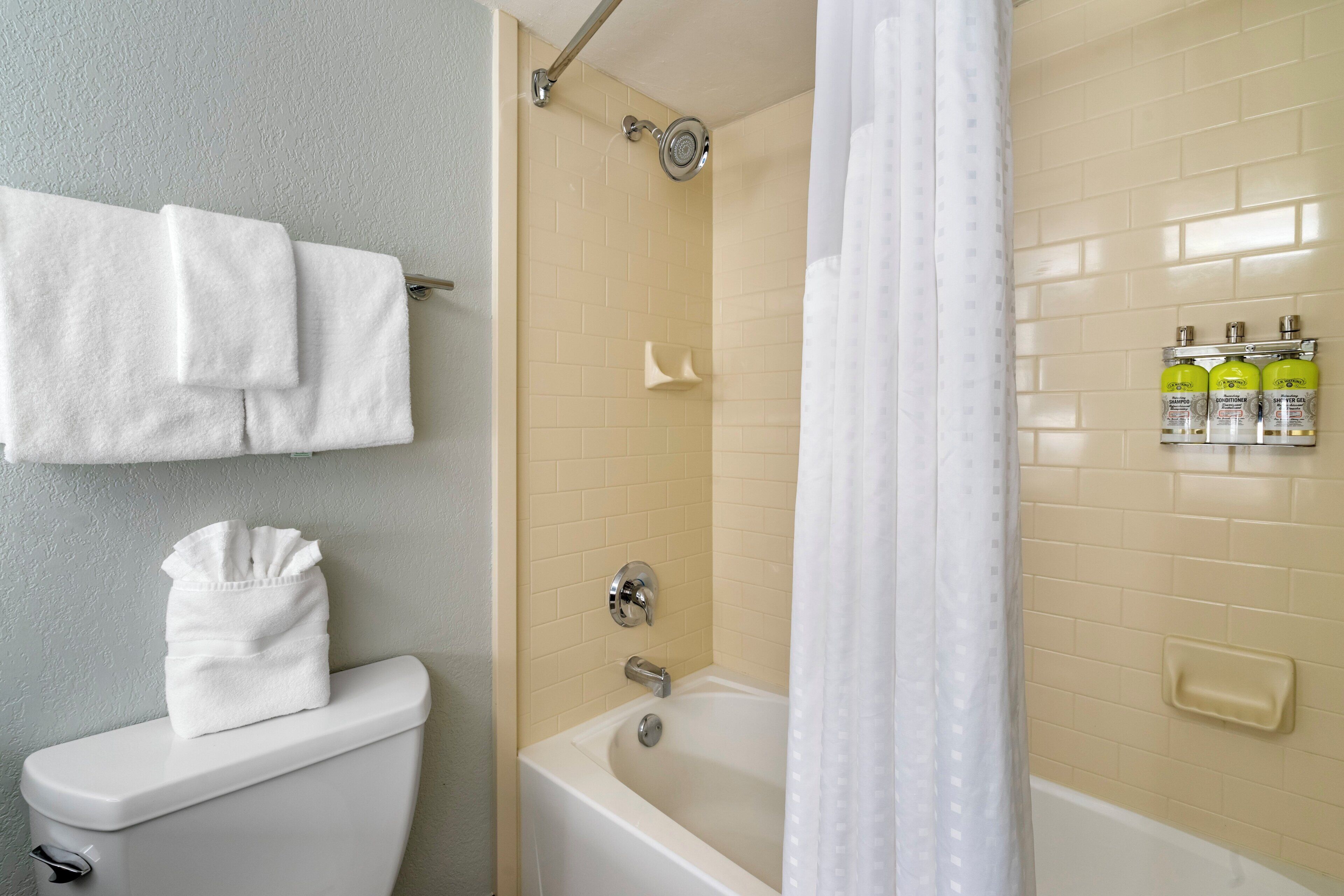 Une salle de bain équipée de toilettes, d’une baignoire, d’un rideau de douche et d’un présentoir mural pour les articles de toilette.