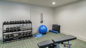 Un gimnasio con equipo de ejercicio, incluyendo mancuernas, una pelota de ejercicios azul y un banco.