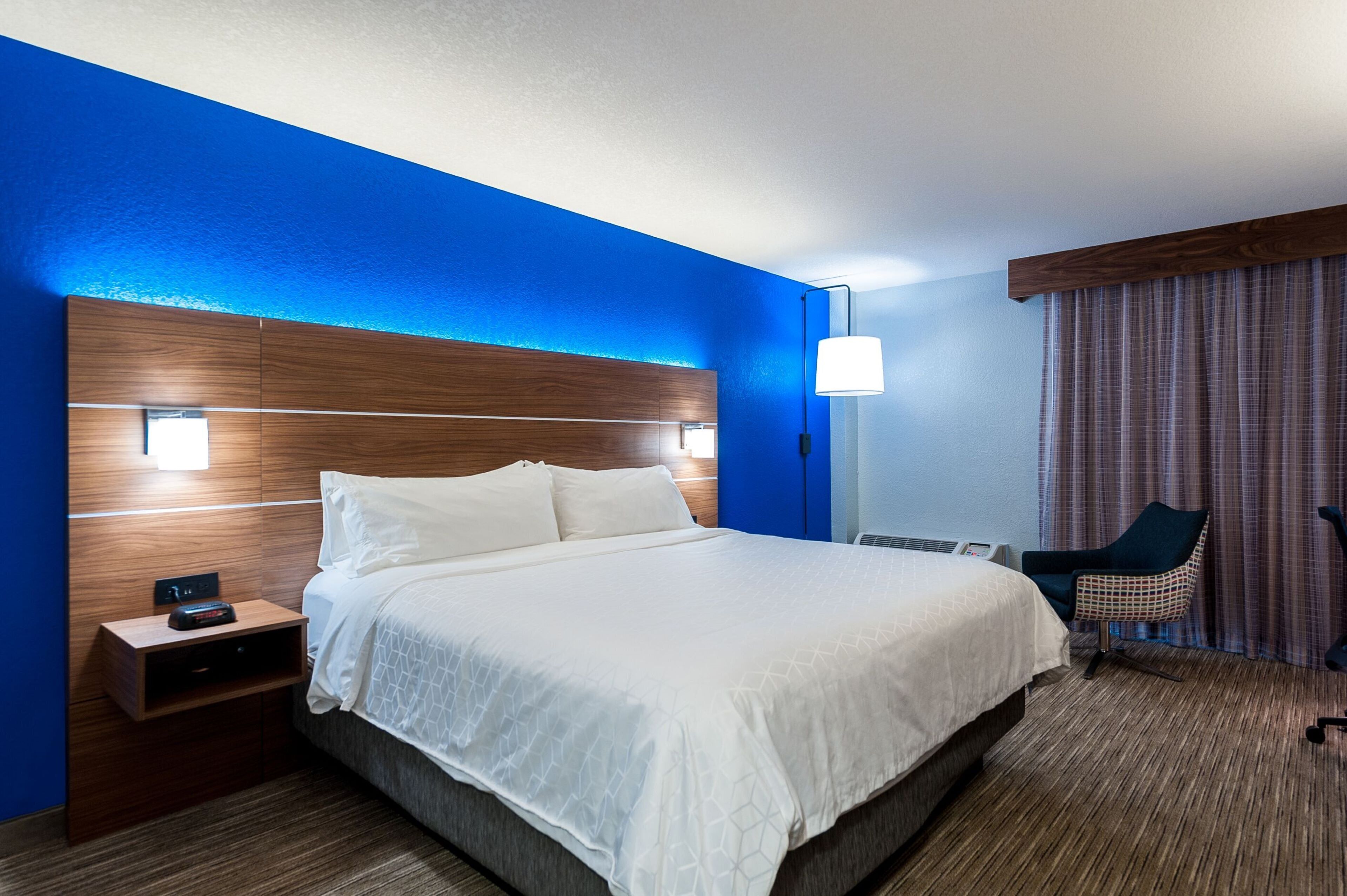 A hotel room with a large bed, a nightstand, a chair, and a lamp.