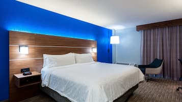 A hotel room with a large bed, a nightstand, a chair, and a lamp.