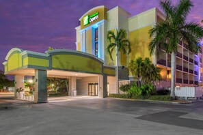 A Holiday Inn Express building with a clear entrance, palm trees, and a purple sky. - Holiday Inn Express Cape Coral-Fort Myers Area by IHG (Cape Coral)