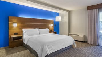 A hotel room with a large bed, a nightstand, a wall-mounted lamp, and a window with curtains.