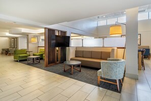 Un moderno vestíbulo de hotel con un sofá, sillas, un televisor y un comedor.