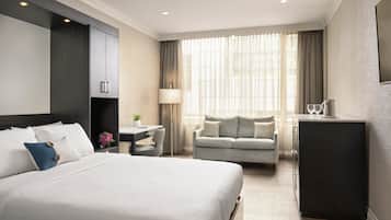 A hotel room with a large bed, a desk, a sofa, and a minibar.