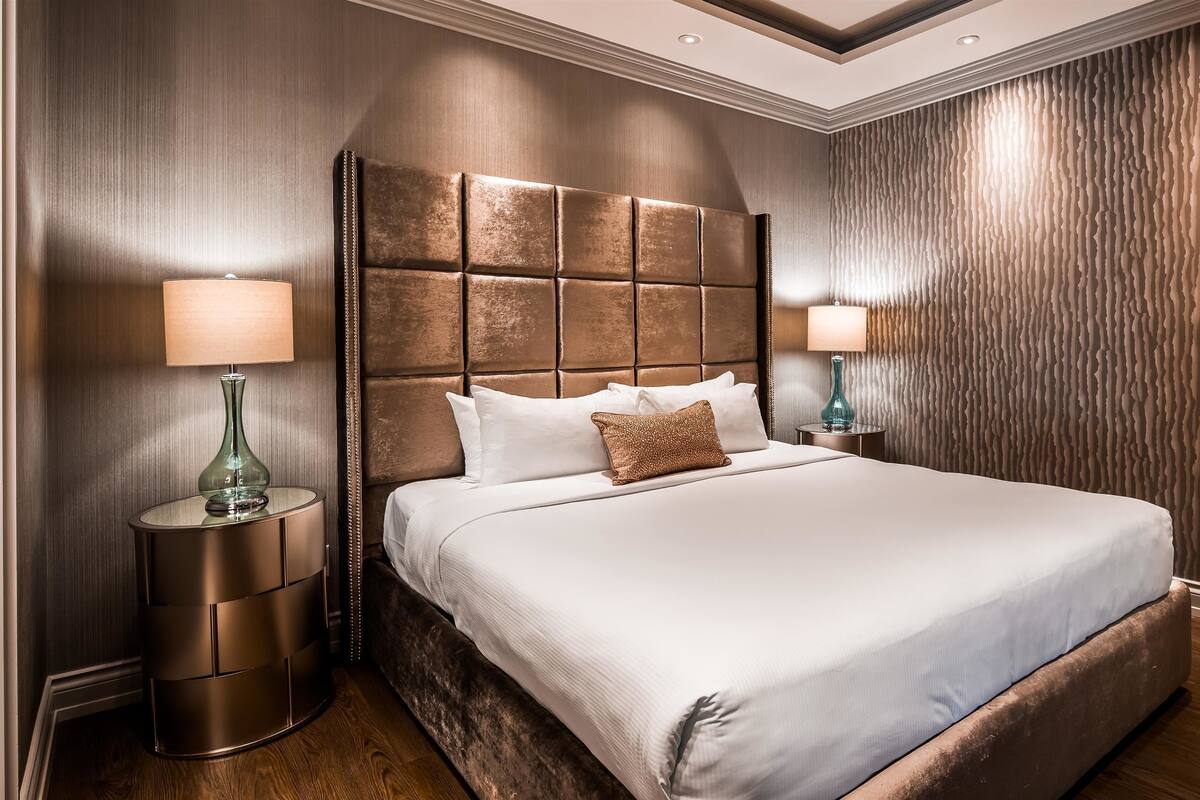 A large bed with a tufted headboard, two bedside tables with lamps, and a textured wall.