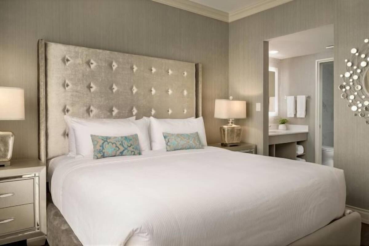 A large bed with a tufted headboard, two bedside tables with lamps, a mirror, and a built-in shelf.