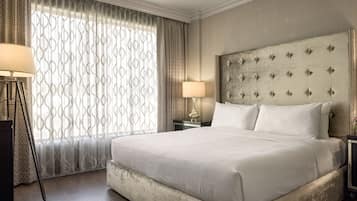 Una cama grande con cabecera capitonada, una lámpara de noche y una cortina estampada.