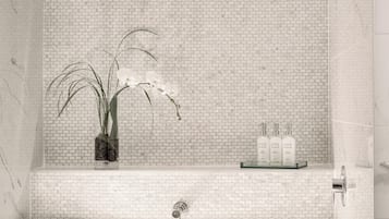 Un baño moderno con una bañera independiente, un estante de vidrio con artículos de tocador y un jarrón con orquídeas.