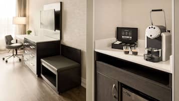 A modern hotel room with a flat-screen TV, a coffee machine, and a small seating area with a desk and chair.