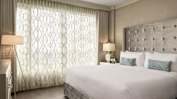 Una habitación de hotel con una cama grande, una mesita de noche con lámpara y una ventana con cortinas estampadas.
