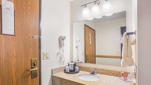 A bathroom with a wooden door, a sink, a mirror, and a hairdryer. - Econo Lodge Cedar Rapids South (Cedar Rapids)