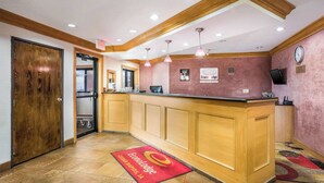 A reception area with a wooden reception desk, a clock, and a digital screen on the wall. - Econo Lodge Cedar Rapids South (Cedar Rapids)
