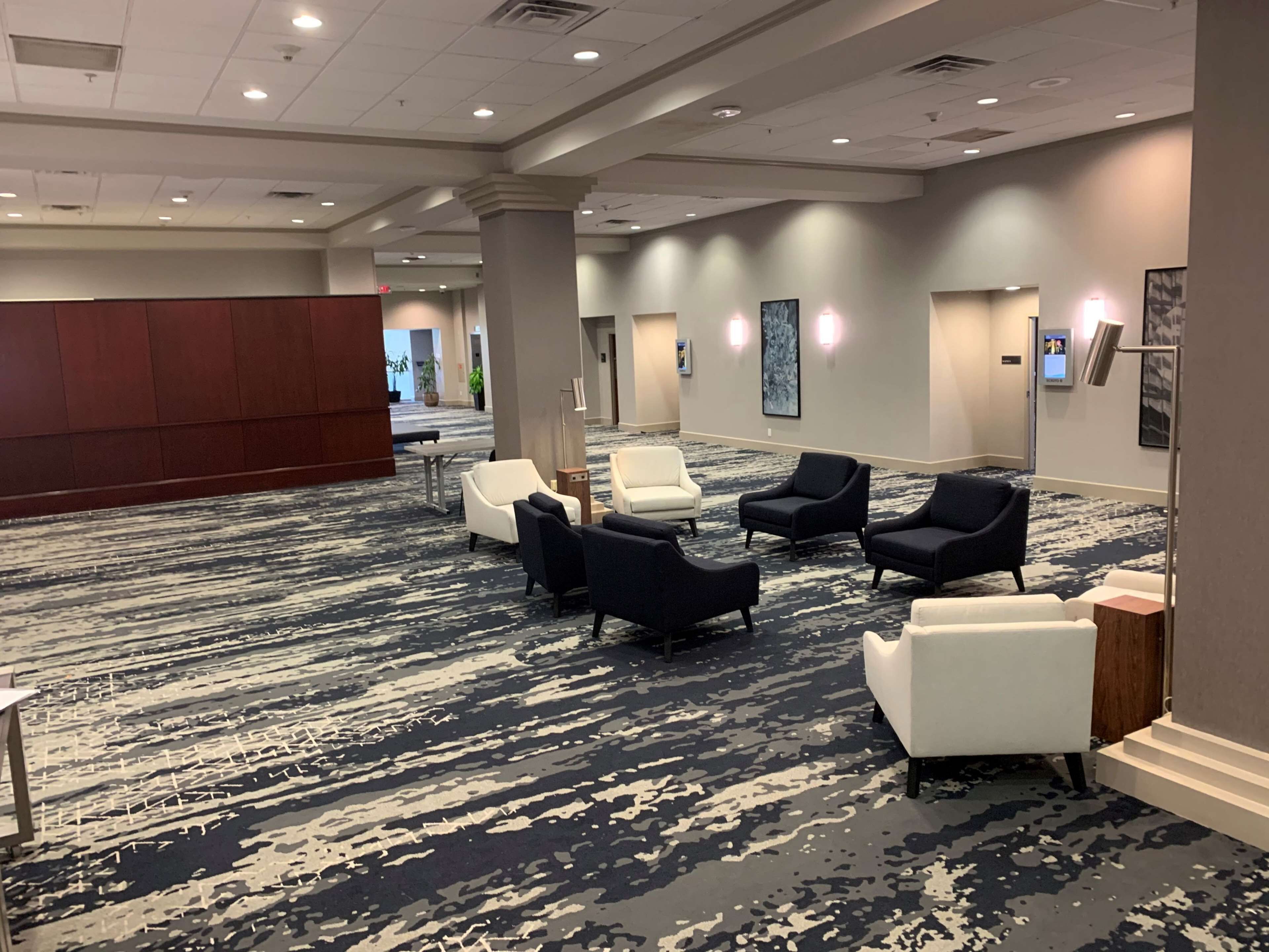 A spacious lobby with a patterned carpet, several seating areas with chairs, and a large pillar.