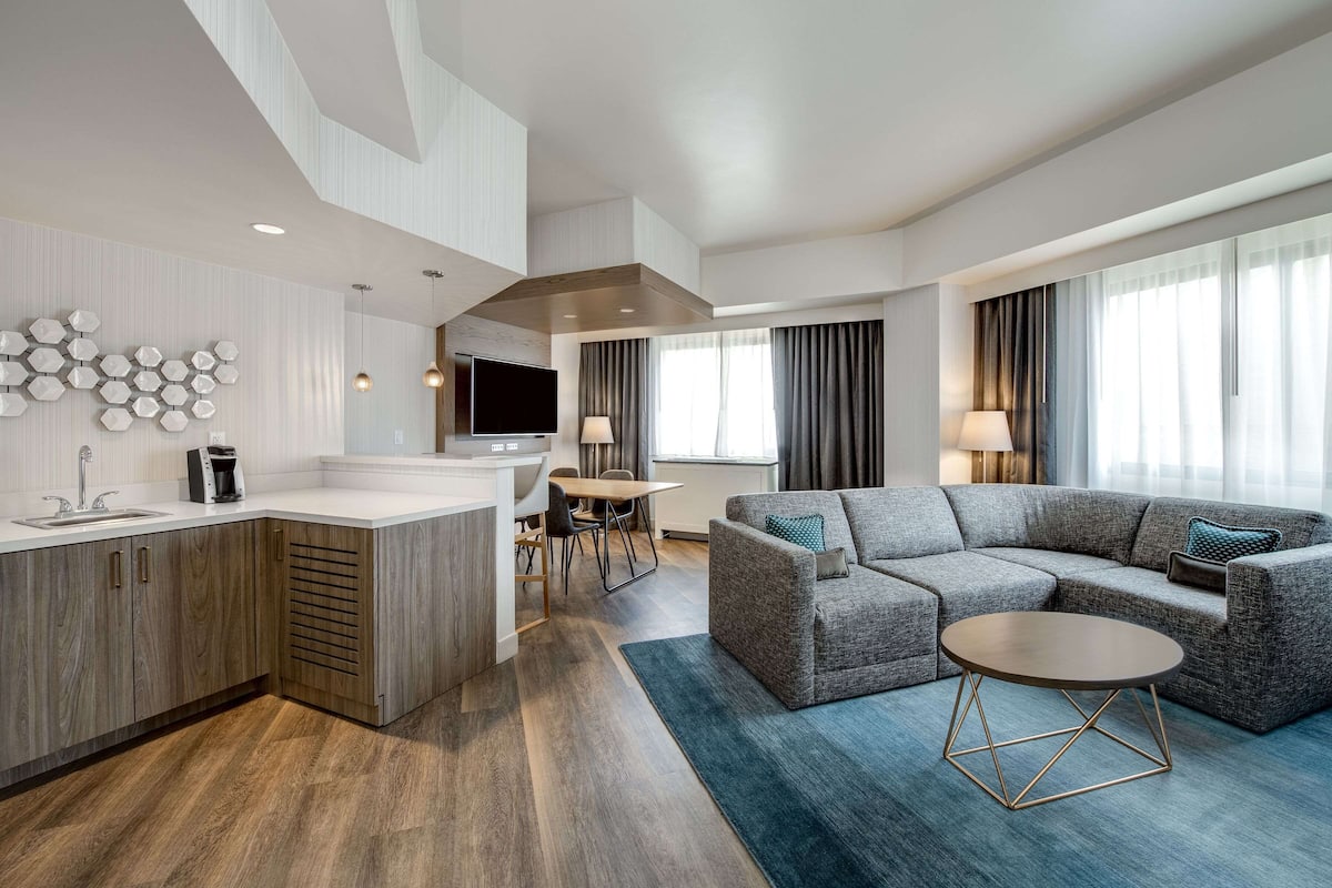 Quarto de hotel moderno com cozinha, um sofá cinza e uma mesa de jantar.