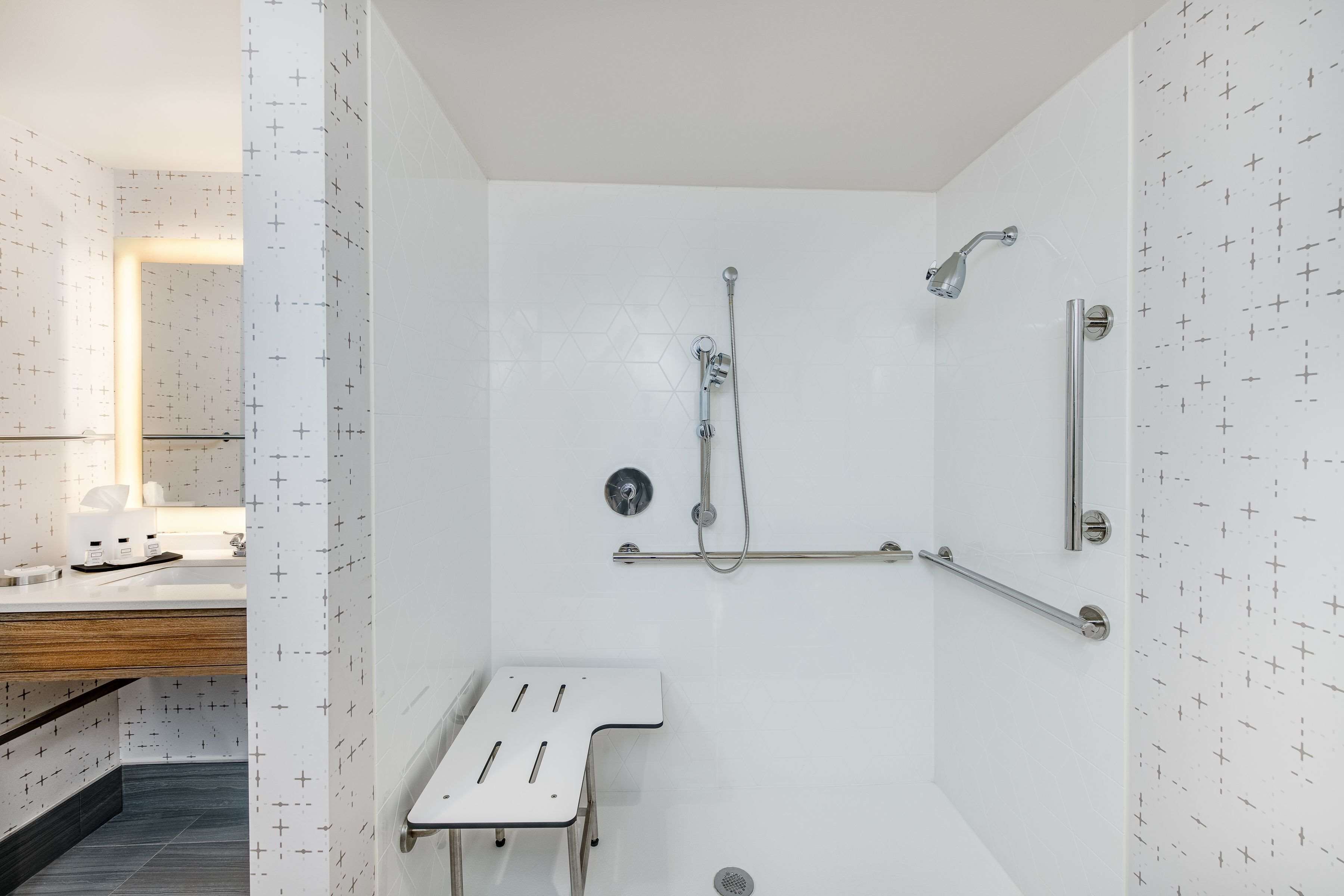 A modern bathroom with a shower, grab bars, and a white sink.