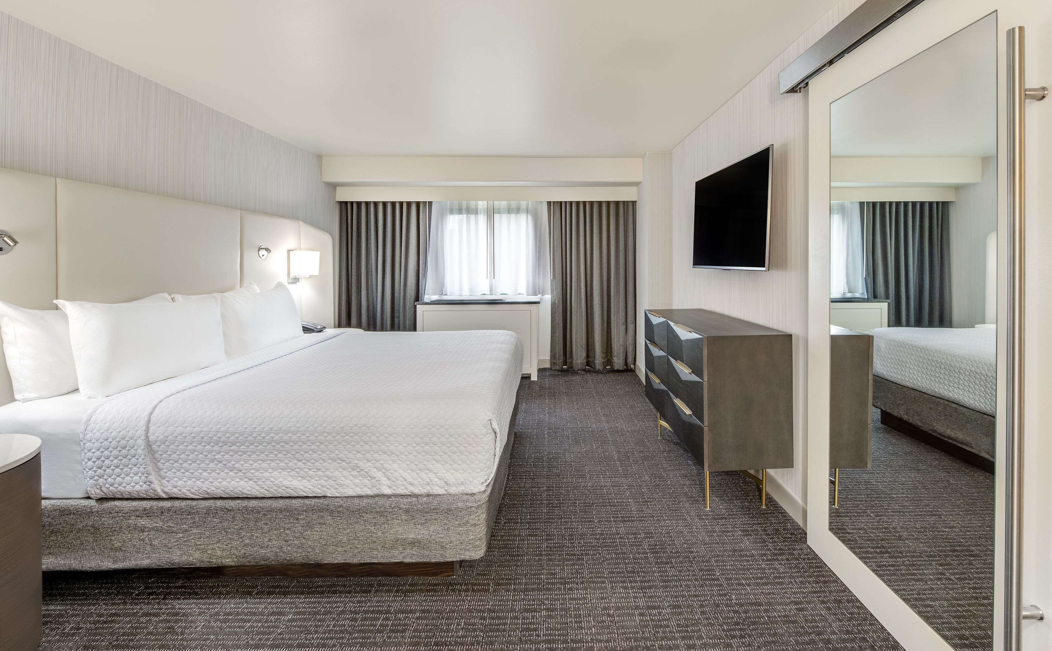 Una habitación de hotel con una cama grande, un televisor de pantalla plana, un aparador y un espejo.