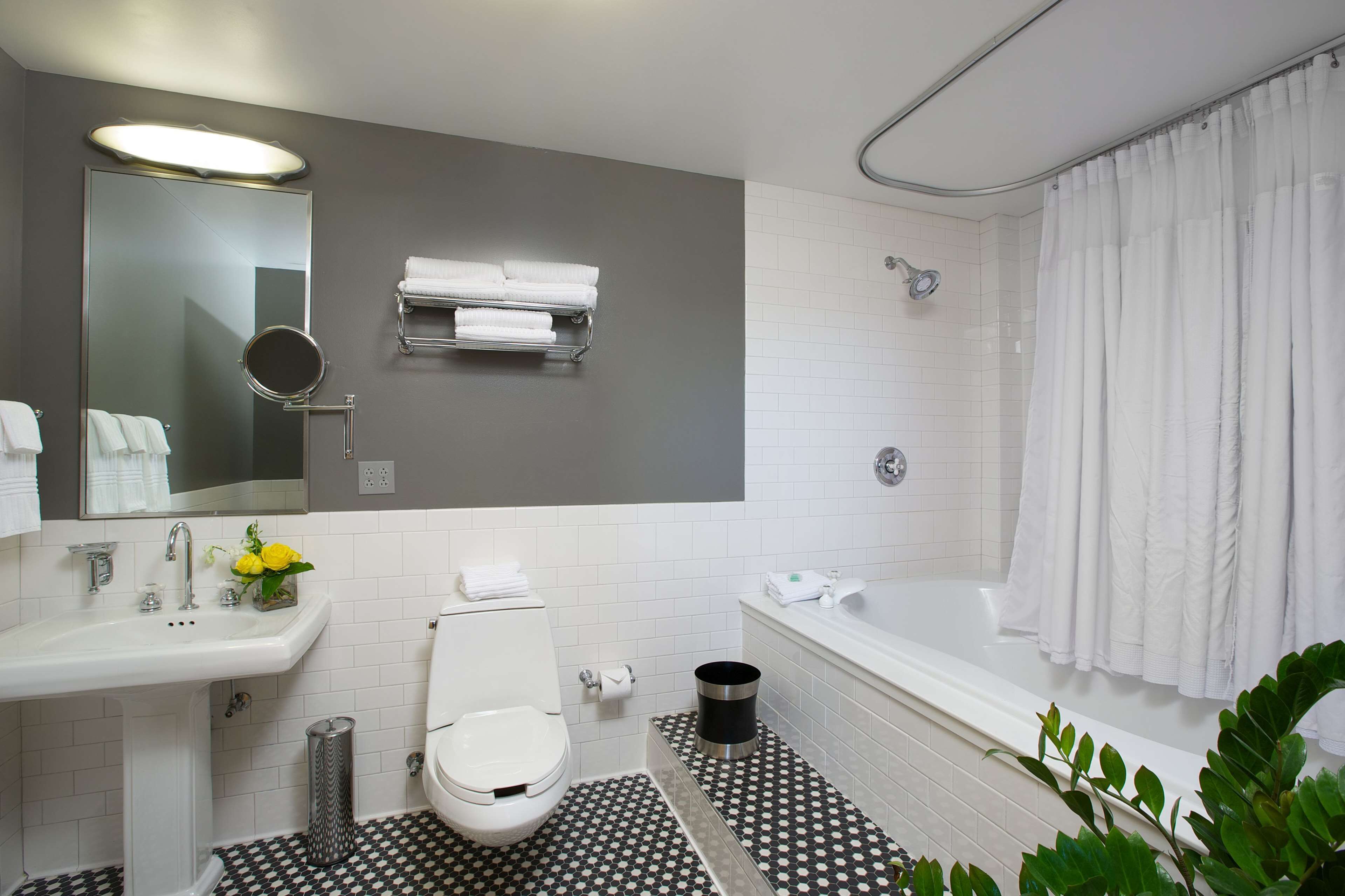Ein Badezimmer mit Waschbecken, Toilette und Badewanne. Über dem Waschbecken befindet sich ein Spiegel, über der Toilette ein Handtuchhalter.