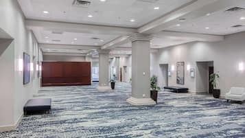 A spacious hotel lobby with a patterned carpet, large pillars, and a wooden panel wall.