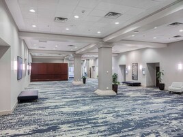 A spacious hotel lobby with a patterned carpet, large pillars, and a wooden panel wall.