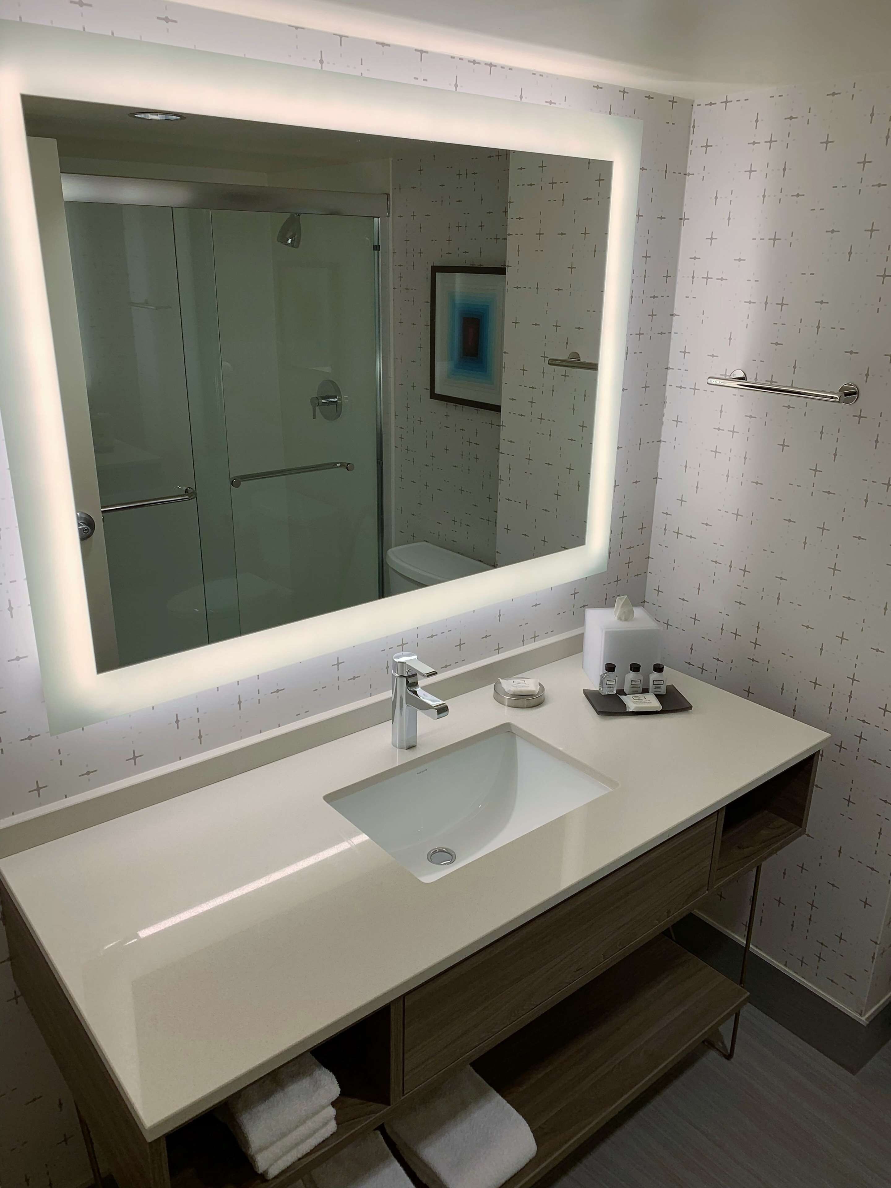 A modern bathroom with a large mirror, a white sink, and a glass shower enclosure.