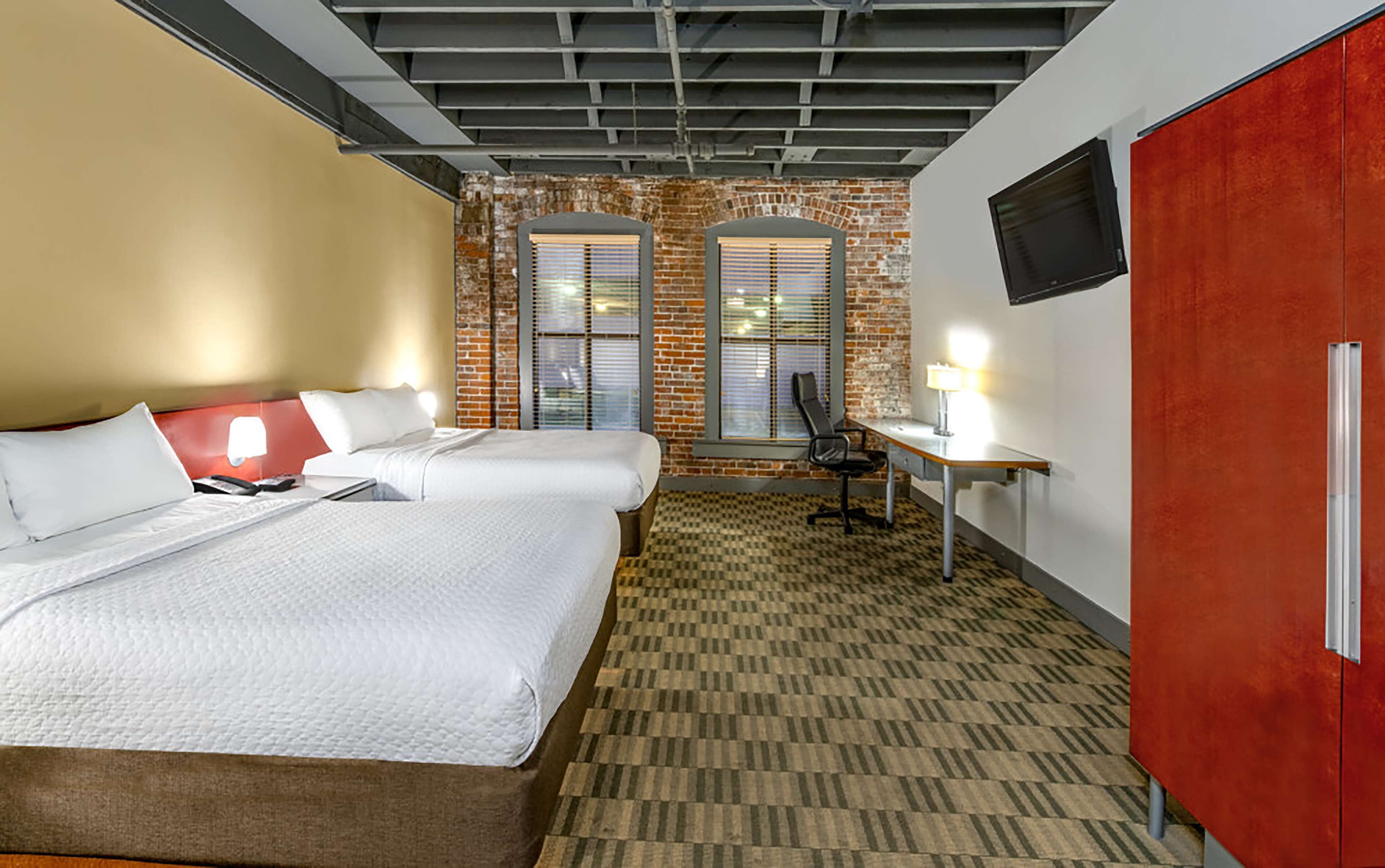 A hotel room with two beds, a desk, a chair, a TV, and a red wardrobe.