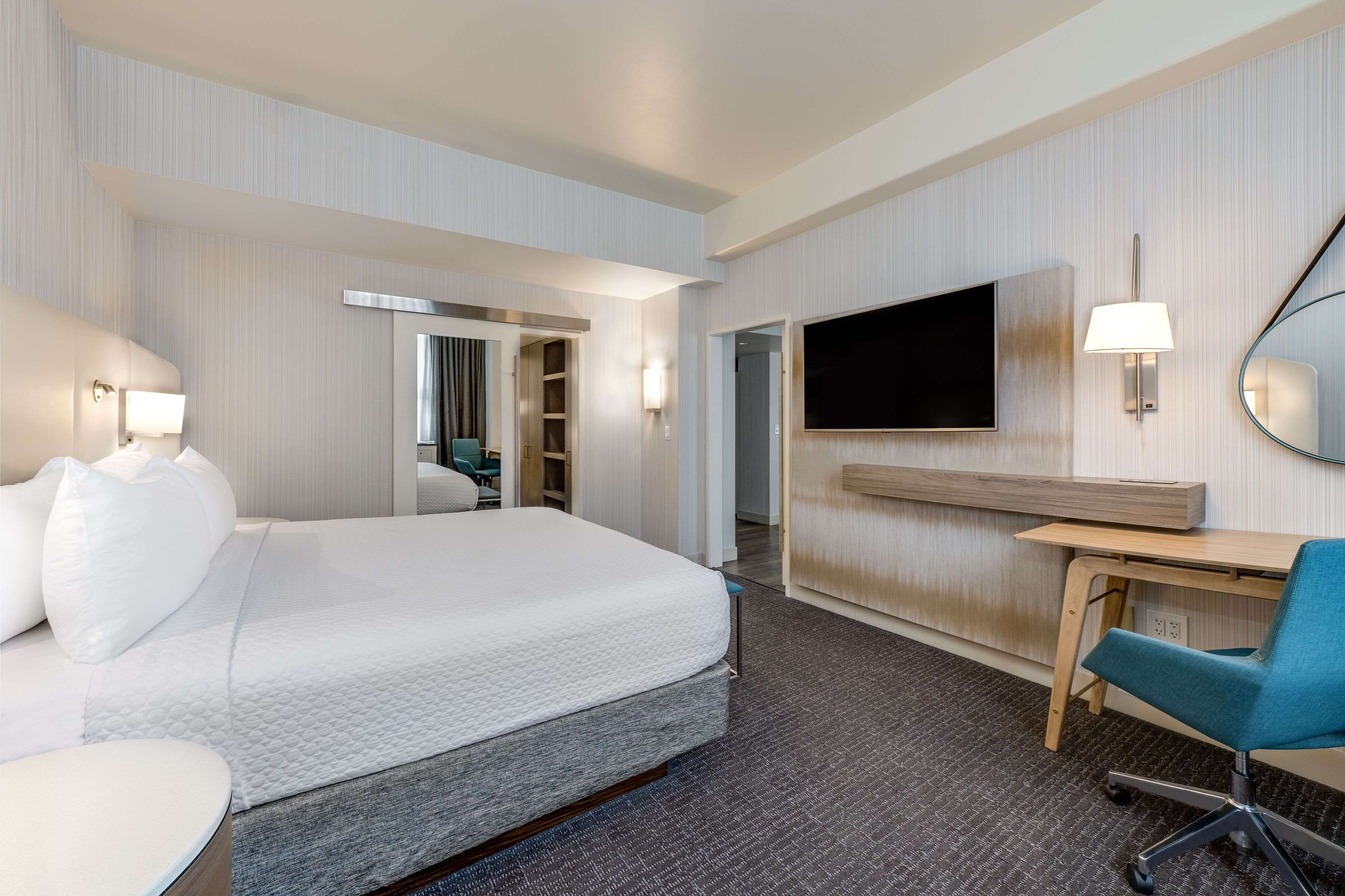 A hotel room with a bed, a desk, a chair, a TV, and a mirror.
