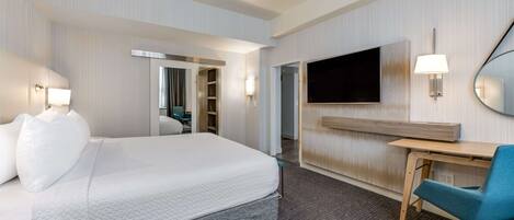 A hotel room with a bed, a desk, a chair, a TV, and a mirror.