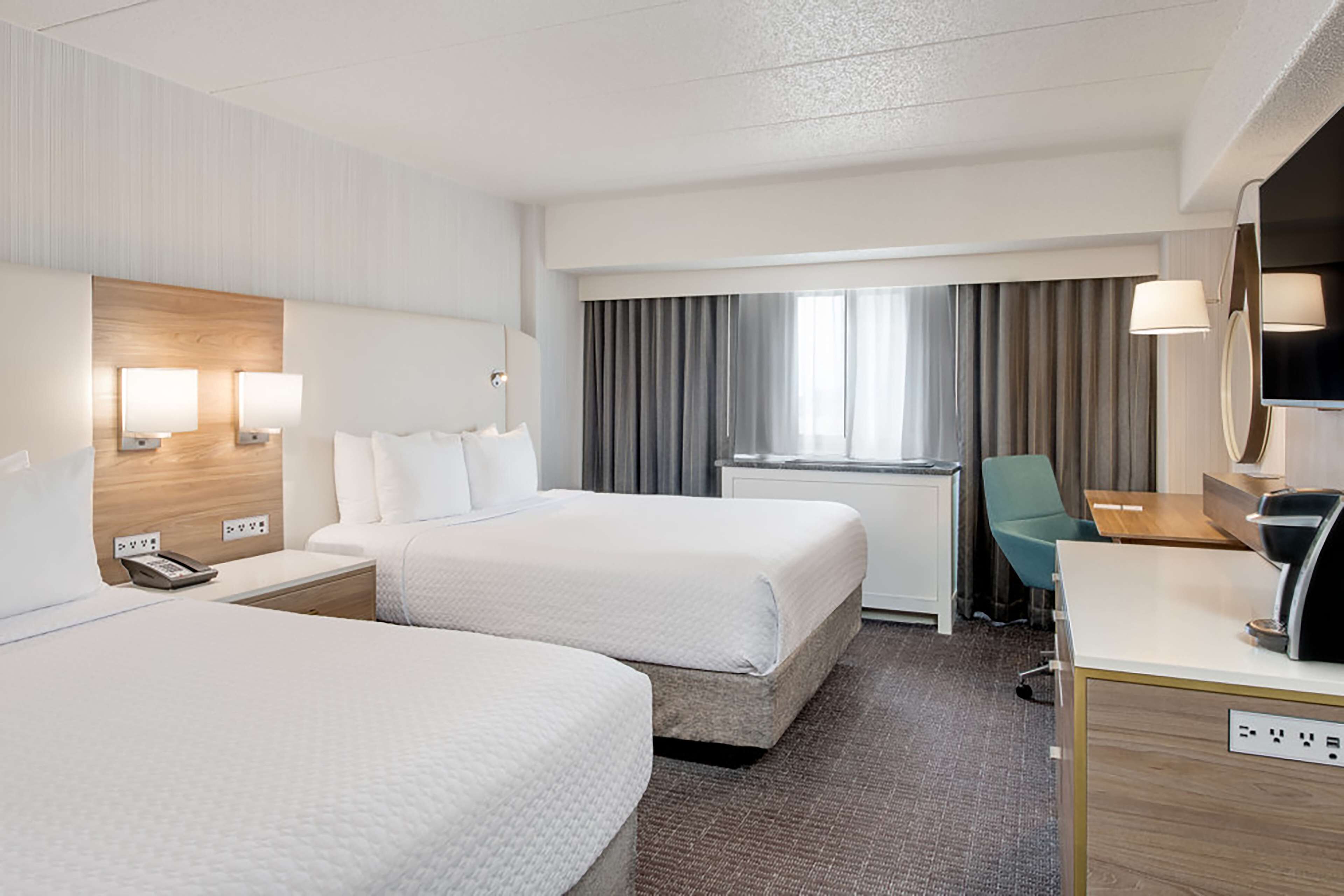 A hotel room with two beds, a desk, a chair, a TV, and a window with curtains.