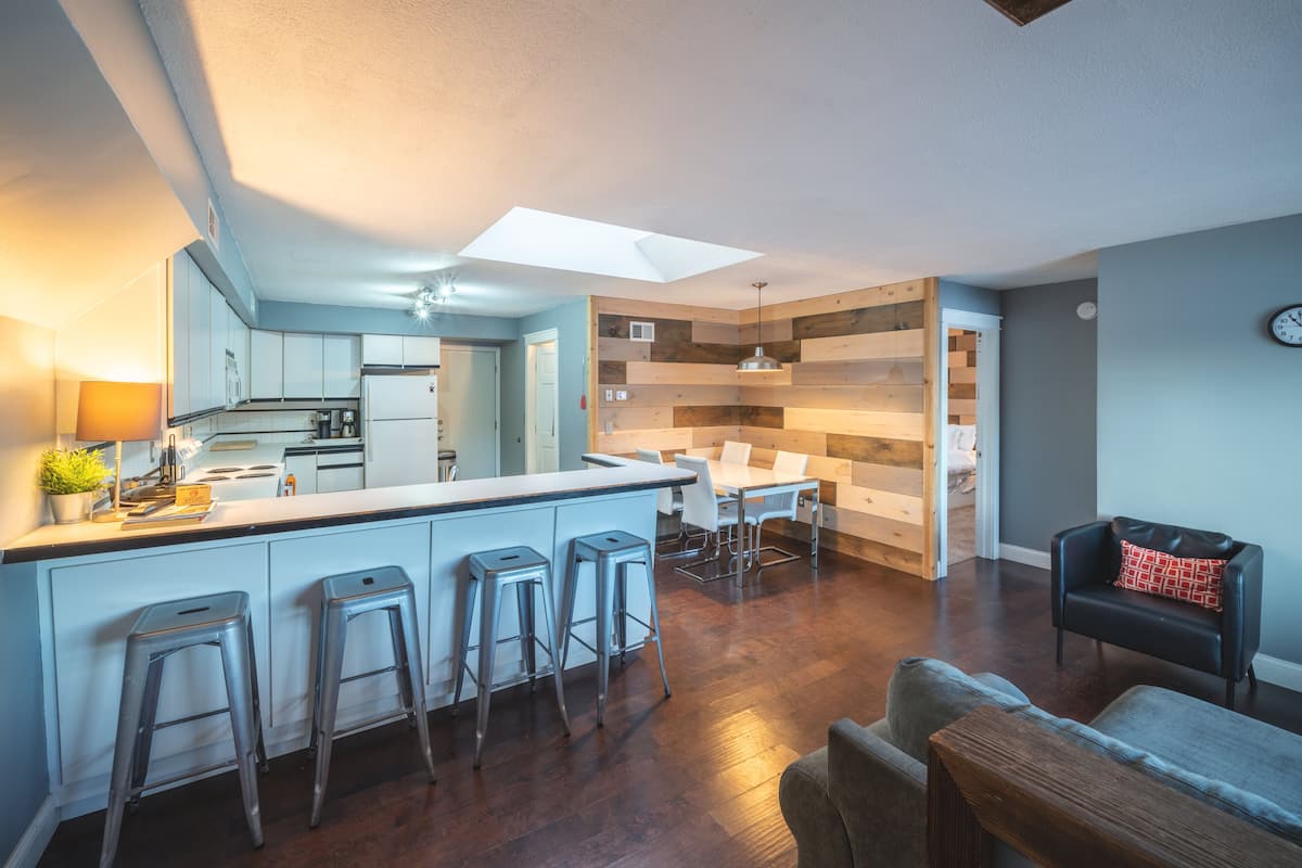 A modern kitchen with a central island, bar stools, and a dining area with a table and chairs.