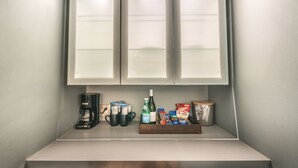 A kitchenette with a coffee maker, mugs, a bottle of water, and packaged snacks. - Hotel Rapids (Grand Rapids)